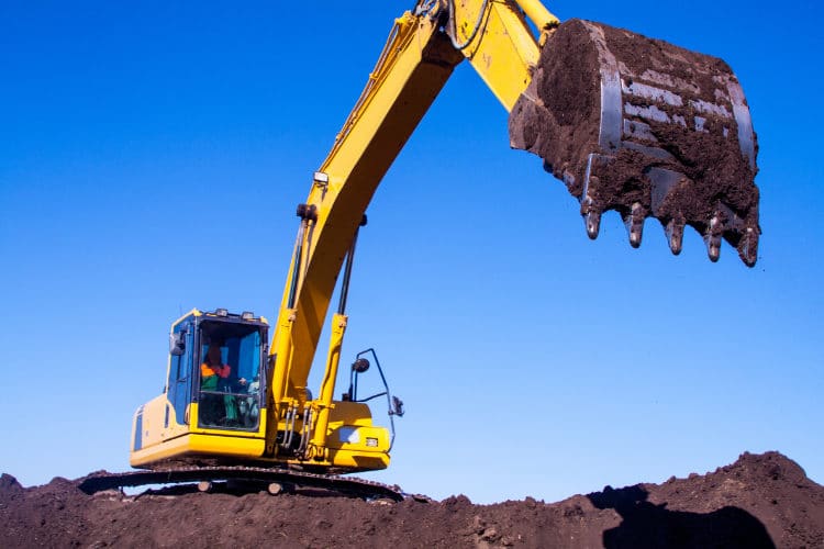 Excavator digging dirt on slope at construction site