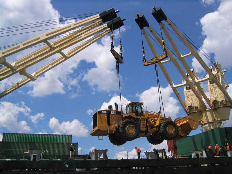 Heavy machinery loader lifted by two cranes at port