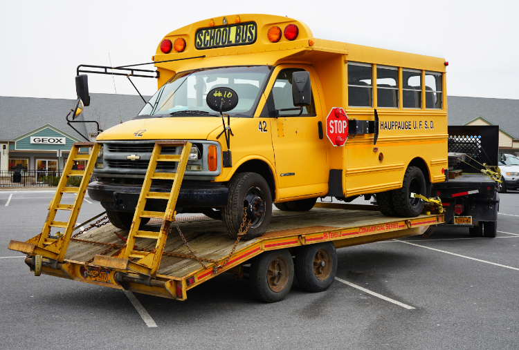 Yellow school bus towed on flatbed trailer